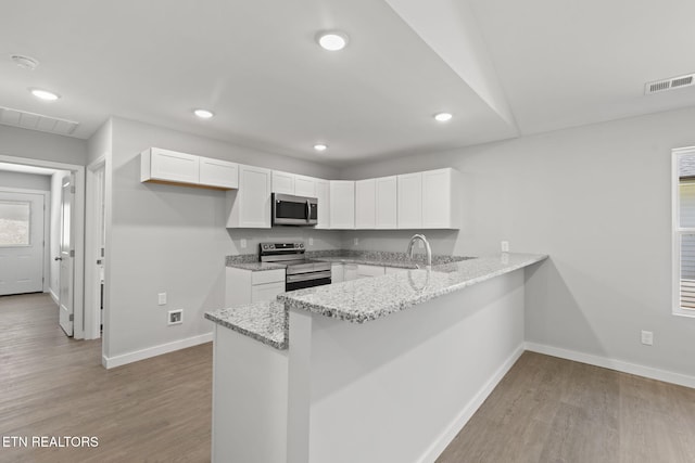 1219 NW Dakota Ave, Knoxville, TN 37921 - kitchen with appliances with stainless steel finishes, a peninsula, white cabinetry, light wood-style flooring, and baseboards