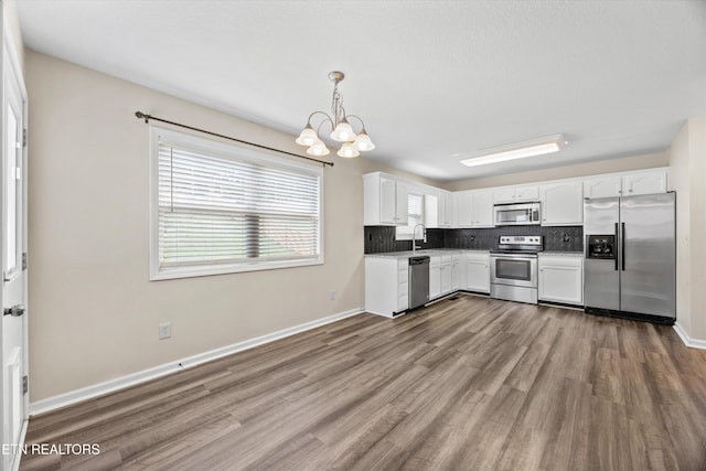 9934 Thunderbolt Way, Knoxville, TN 37923 - kitchen with appliances with stainless steel finishes, a chandelier, wood finished floors, white cabinetry, and tasteful backsplash