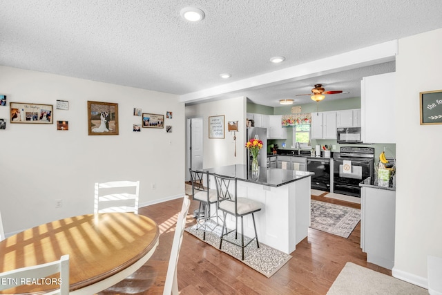 6608 Hickory Way Ln, Knoxville, TN 37918 - kitchen featuring black appliances, a textured ceiling, white cabinetry, dark countertops, and a breakfast bar