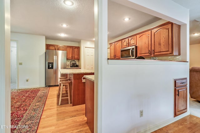 45 Calderwood Cir, Fairfield Glade, TN 38558 - kitchen with appliances with stainless steel finishes, light wood-style floors, a breakfast bar area, light stone counters, and brown cabinetry
