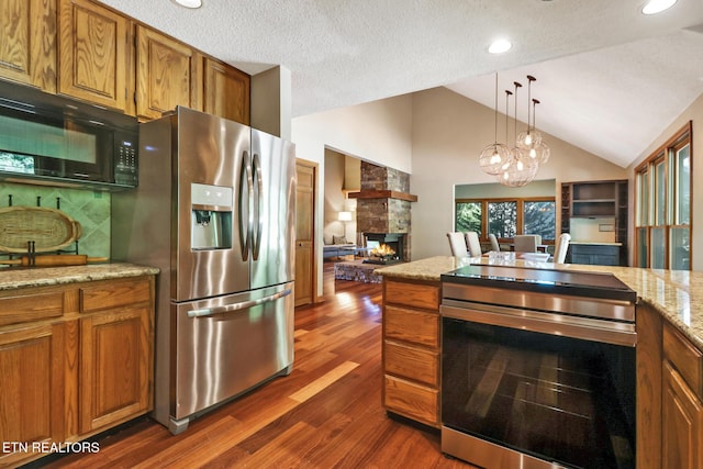 104 Maltese Ln, Oak Ridge, TN 37830 - kitchen featuring appliances with stainless steel finishes, brown cabinetry, a stone fireplace, dark wood-style floors, and lofted ceiling