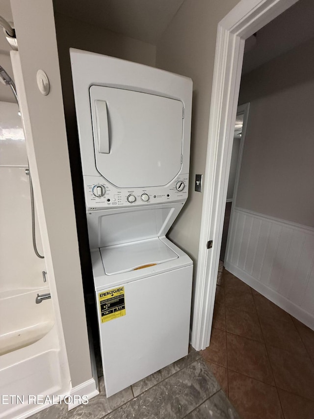 304 Douglas Ave, Knoxville, TN 37921 - laundry room featuring stacked washer and clothes dryer, dark tile patterned floors, and a wainscoted wall