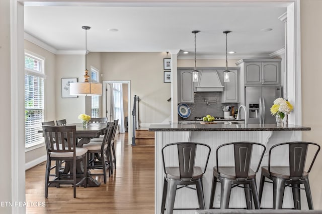 12332 Bonnybridge Ln, Knoxville, TN 37922 - kitchen featuring stainless steel refrigerator with ice dispenser, custom exhaust hood, a breakfast bar, crown molding, and light wood-style flooring