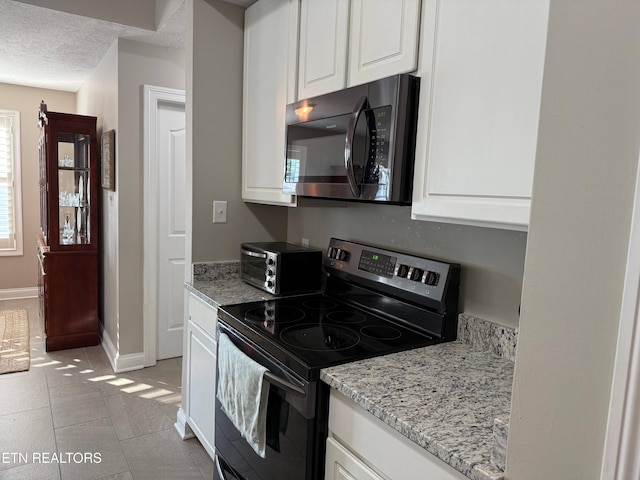 7243 Autumn View Ln, Powell, TN 37849 - kitchen featuring black microwave, electric range, white cabinets, baseboards, and light stone counters