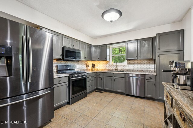 7901 Ewing Rd, Powell, TN 37849 - kitchen with appliances with stainless steel finishes, gray cabinetry, a sink, backsplash, and light stone countertops