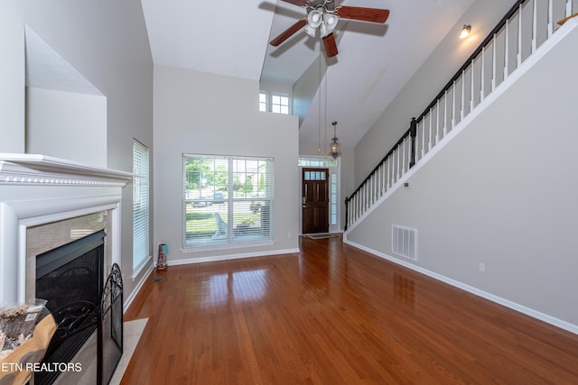 9100 Sway Branch Ln, Knoxville, TN 37922 - unfurnished living room with a towering ceiling, a ceiling fan, a tile fireplace, stairs, and wood finished floors