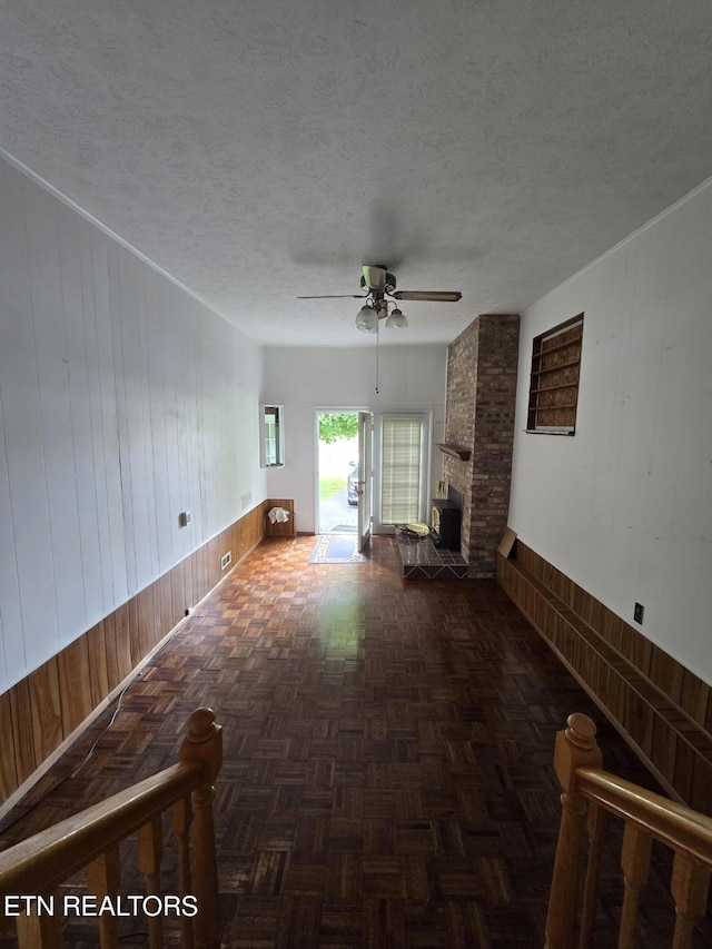 114 Verdun Rd, Oneida, TN 37841 - unfurnished living room with wooden walls, a ceiling fan, a fireplace, a textured ceiling, and wainscoting
