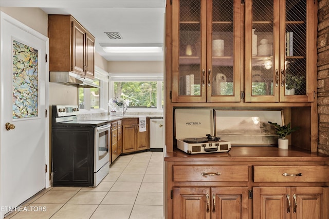 386 E Dr, Oak Ridge, TN 37830 - kitchen featuring stainless steel electric stove, under cabinet range hood, brown cabinetry, light tile patterned flooring, and glass insert cabinets