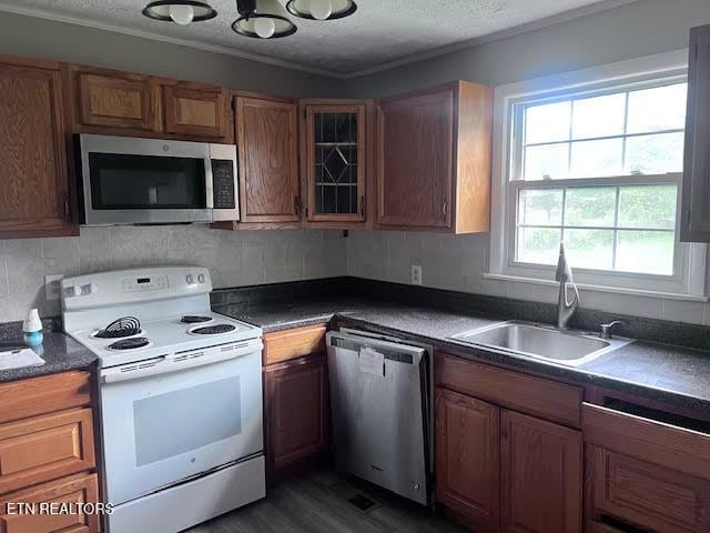 7832 Brickyard Rd, Powell, TN 37849 - kitchen with stainless steel appliances, a sink, dark countertops, brown cabinetry, and crown molding