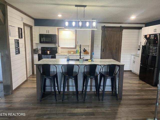 203 Baker Cir, Maynardville, TN 37807 - kitchen with black appliances, a barn door, white cabinetry, a breakfast bar area, and wooden walls