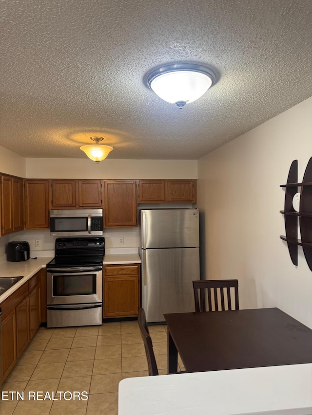 7925 Eldin Way, Powell, TN 37849 - kitchen with stainless steel appliances, a textured ceiling, light countertops, brown cabinets, and light tile patterned flooring
