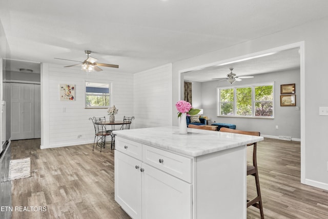 3408 Hackberry Rd, Knoxville, TN 37931 - kitchen featuring a ceiling fan, a breakfast bar, light wood-type flooring, white cabinetry, and wooden walls