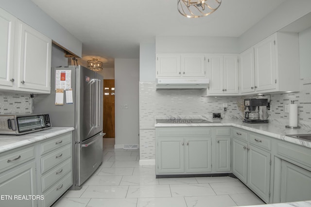 506 Blockhouse Valley Rd, Clinton, TN 37716 - kitchen with under cabinet range hood, light marble finish floors, decorative backsplash, freestanding refrigerator, and white cabinetry