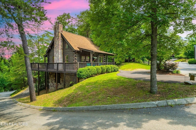 664 Kings Hills Blvd, Pigeon Forge, TN 37863 - property exterior at dusk with a deck, a yard, a chimney, log siding, and stone siding