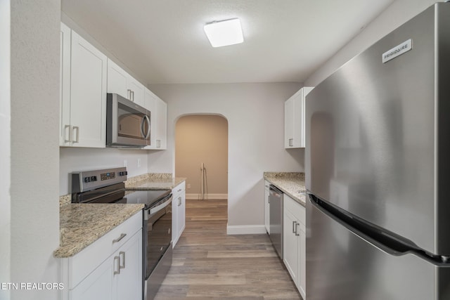 406 S Indiana Ave, Lafollette, TN 37766 - kitchen featuring appliances with stainless steel finishes, arched walkways, light wood-style flooring, white cabinetry, and light stone countertops