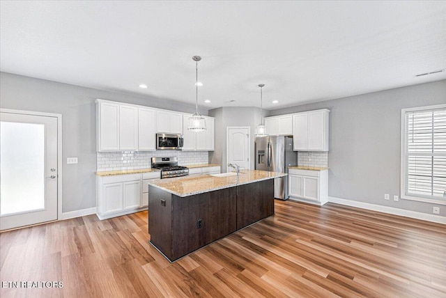 8630 Yellow Aster Rd, Knoxville, TN 37931 - kitchen featuring stainless steel appliances, light wood-style flooring, tasteful backsplash, white cabinetry, and a center island with sink