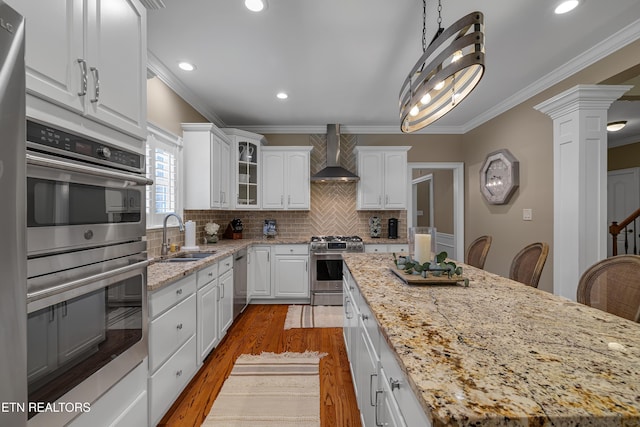 920 Andover View Ln, Knoxville, TN 37922 - kitchen featuring appliances with stainless steel finishes, wall chimney range hood, white cabinets, a center island, and ornamental molding