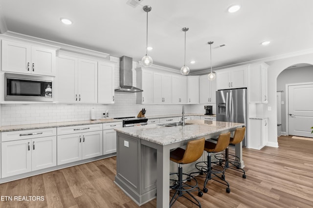 402 Sycamore Pl, Loudon, TN 37774 - kitchen featuring wall chimney range hood, stainless steel appliances, arched walkways, white cabinetry, and a kitchen island with sink