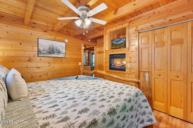 2217 Red Bud Rd, Sevierville, TN 37876 - bedroom with a wooden ceiling with exposed beams, wood walls, light wood finished floors, a closet, and a multi sided fireplace