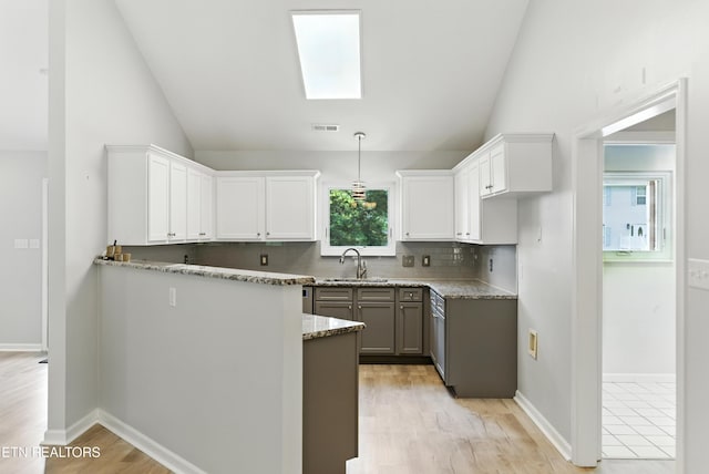 8808 Cedar Springs Ln, Knoxville, TN 37923 - kitchen featuring vaulted ceiling, backsplash, light stone counters, a skylight, and white cabinets