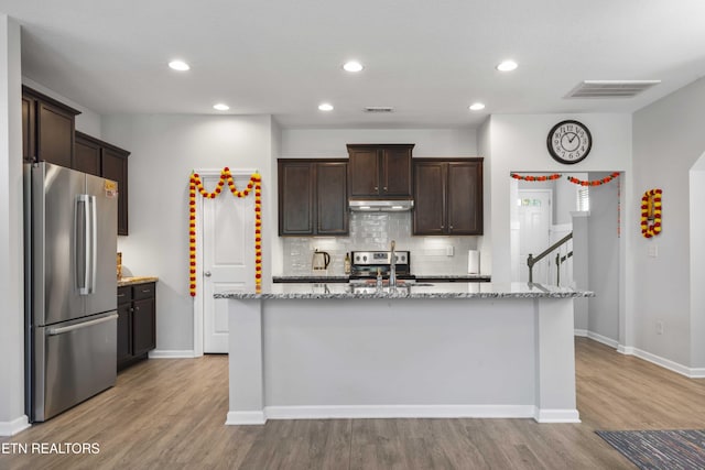 10703 Grantham Ln, Knoxville, TN 37932 - kitchen featuring appliances with stainless steel finishes, under cabinet range hood, dark brown cabinetry, decorative backsplash, and light wood-style flooring