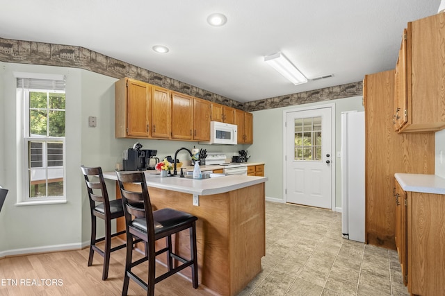 814 Plantation Dr, Pigeon Forge, TN 37863 - kitchen with white appliances, a peninsula, light countertops, a kitchen bar, and brown cabinetry