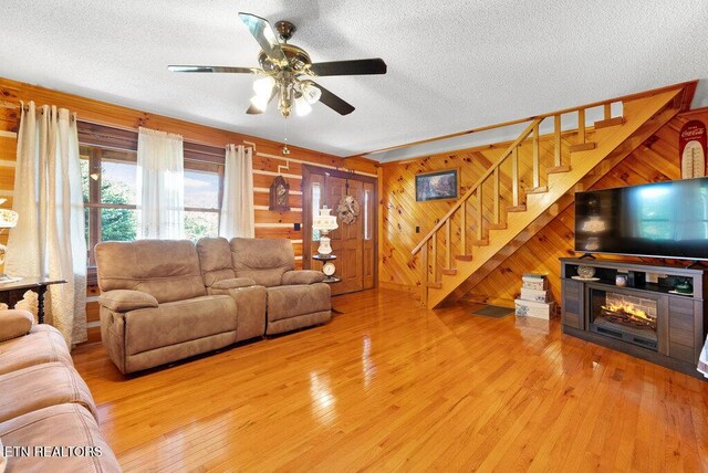 1821 S Nopone Valley Rd, Decatur, TN 37322 - living room featuring a textured ceiling, stairs, light wood finished floors, a ceiling fan, and wood walls