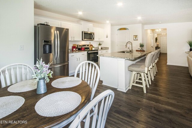 7408 Game Bird St, Corryton, TN 37721 - kitchen featuring appliances with stainless steel finishes, white cabinetry, a kitchen island with sink, dark wood finished floors, and a breakfast bar