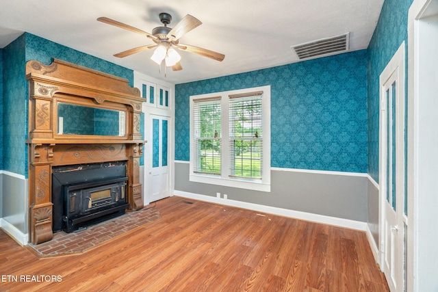 2115 Aaron Ct, Sevierville, TN 37876 - unfurnished living room featuring wallpapered walls, wood finished floors, ceiling fan, a wood stove, and a wainscoted wall