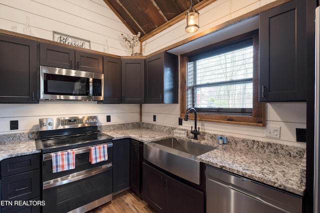 1023 Timberlake Cir, Sevierville, TN 37876 - kitchen featuring stainless steel appliances, vaulted ceiling, wood walls, light stone counters, and light wood-style floors