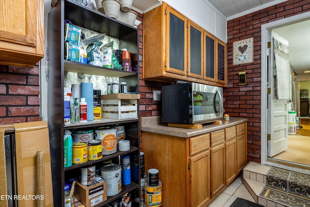 816 Thorn Grove Pike, Strawberry Plains, TN 37871 - kitchen featuring stainless steel microwave, brick wall, brown cabinets, light tile patterned flooring, and glass insert cabinets