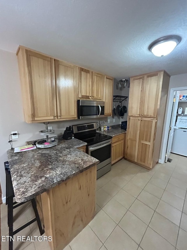 935 Pinetree Rd, Jamestown, TN 38556 - kitchen with appliances with stainless steel finishes, light brown cabinets, light tile patterned flooring, a peninsula, and a breakfast bar area