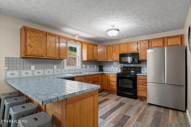 2270 Cove Pointe Rd, Lafollette, TN 37766 - kitchen with black appliances, a peninsula, brown cabinets, light wood-style flooring, and backsplash