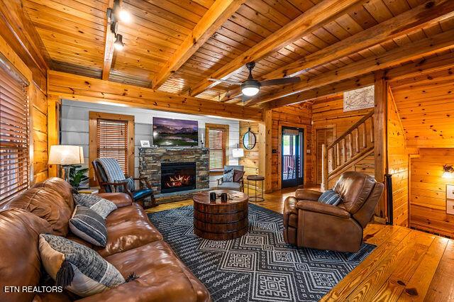 3322 Covered Bridge Way, Sevierville, TN 37862 - living room with hardwood / wood-style flooring, wooden walls, a wooden ceiling with exposed beams, stairs, and a stone fireplace