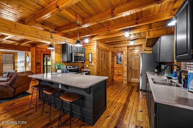3322 Covered Bridge Way, Sevierville, TN 37862 - kitchen featuring dark wood-style flooring, a wood ceiling with exposed beams, a kitchen bar, open floor plan, and wood walls