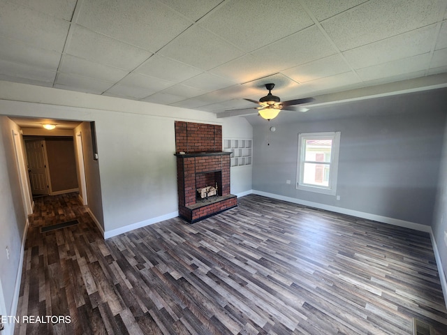 308 E Prospect St, Lafollette, TN 37766 - unfurnished living room with dark wood-type flooring, a brick fireplace, a drop ceiling, and a ceiling fan