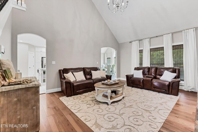 living area featuring arched walkways, high vaulted ceiling, wood finished floors, and a chandelier
