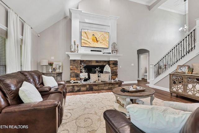 living area featuring arched walkways, wood finished floors, stairway, ornamental molding, and a stone fireplace
