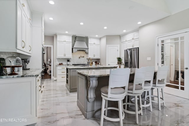 kitchen with a kitchen island, recessed lighting, backsplash, light marble finish floors, and light stone countertops