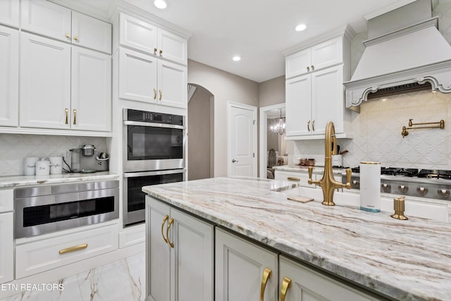 kitchen featuring stainless steel appliances, arched walkways, decorative backsplash, recessed lighting, and white cabinets