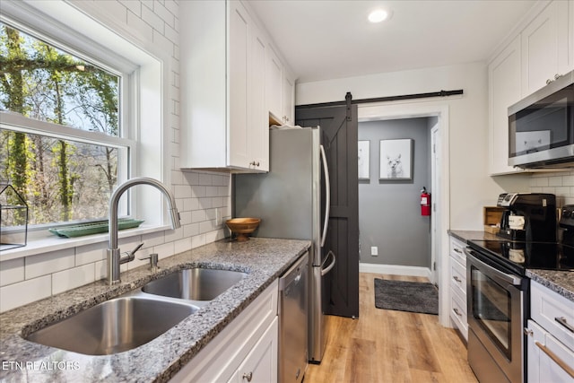 335 Sugar Mountain Way, Pigeon Forge, TN 37863 - kitchen with appliances with stainless steel finishes, a barn door, light wood finished floors, white cabinetry, and backsplash