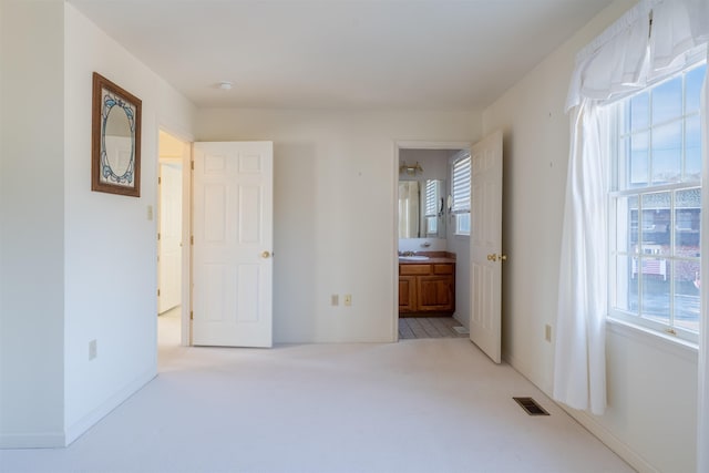 unfurnished bedroom featuring baseboards, visible vents, light colored carpet, ensuite bathroom, and a sink