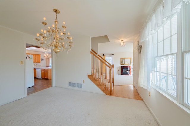 interior space with visible vents, a glass covered fireplace, stairs, carpet flooring, and a chandelier