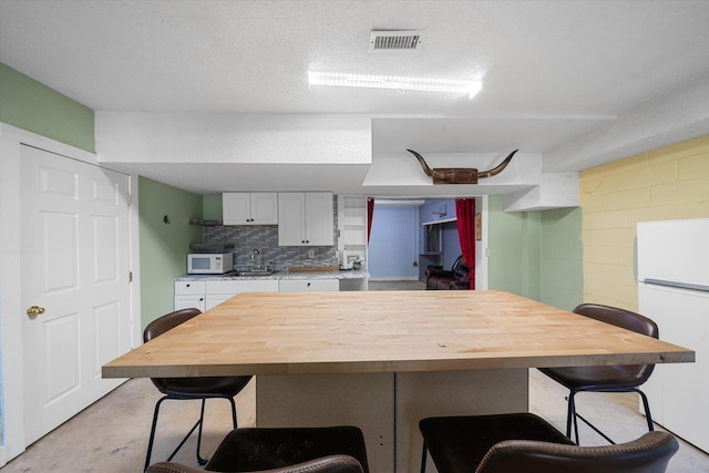 kitchen with a breakfast bar, white appliances, backsplash, white cabinets, and a textured ceiling