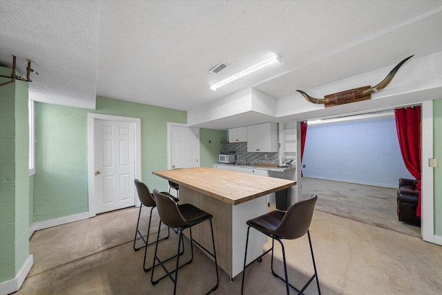 kitchen with wood counters, a center island, white cabinets, a kitchen breakfast bar, and a textured ceiling