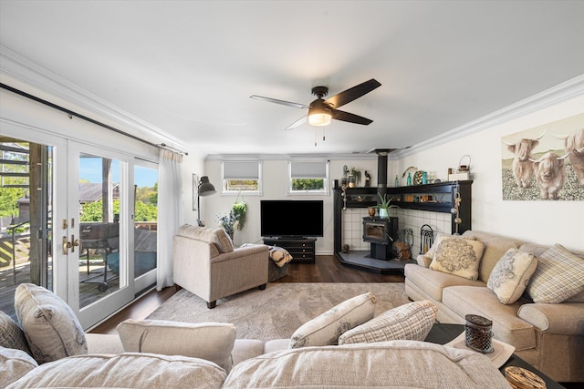 living room featuring french doors, ceiling fan, dark wood-type flooring, crown molding, and a wood stove