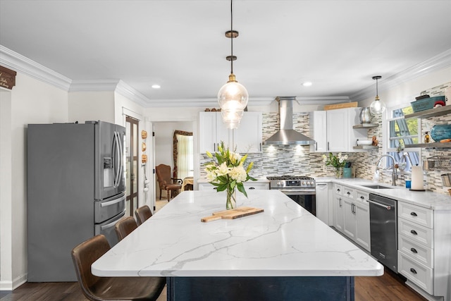 kitchen with wall chimney exhaust hood, stainless steel appliances, pendant lighting, a center island, and white cabinetry