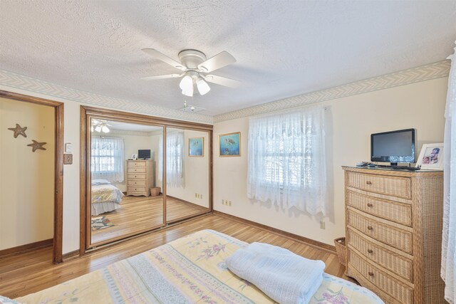 bedroom with light wood-type flooring, baseboards, a textured ceiling, and ceiling fan