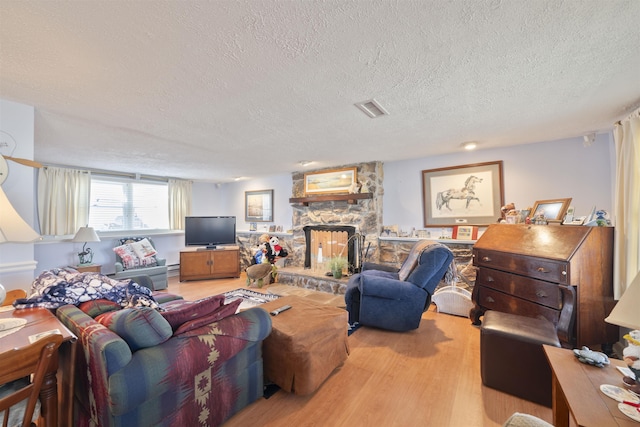 living area featuring wood finished floors, visible vents, a baseboard radiator, a fireplace, and a textured ceiling