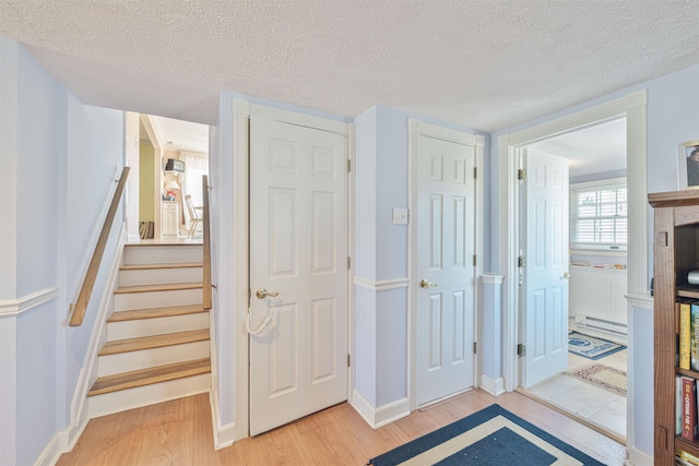 interior space featuring baseboards, stairway, baseboard heating, light wood-style floors, and a textured ceiling